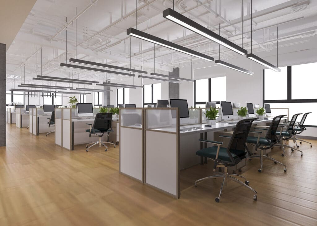 Modern open-plan office refurbishment with rows of workstations, computer monitors, ergonomic task chairs, glass privacy screens, indoor plants, suspended linear lighting and exposed ceiling services.