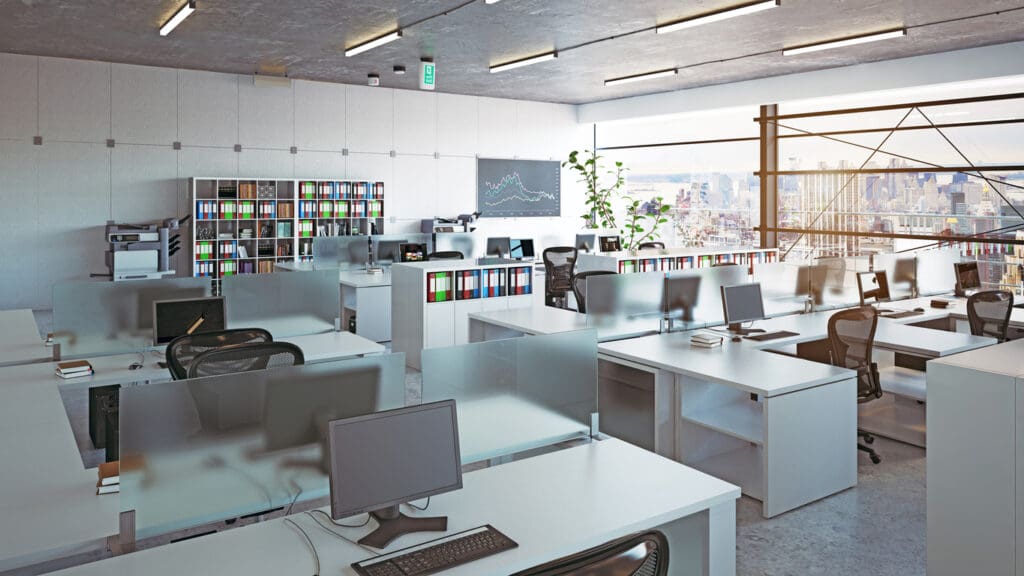 Modern open-plan office fit out with white workstations, frosted desk screens, computer monitors, mesh task chairs, storage shelving, ceiling strip lights and large windows overlooking a city skyline.