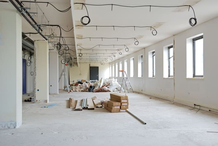 Empty commercial office during Cat A fit out works with exposed electrical cabling, unfinished walls, ladders and construction materials across the open floor space.