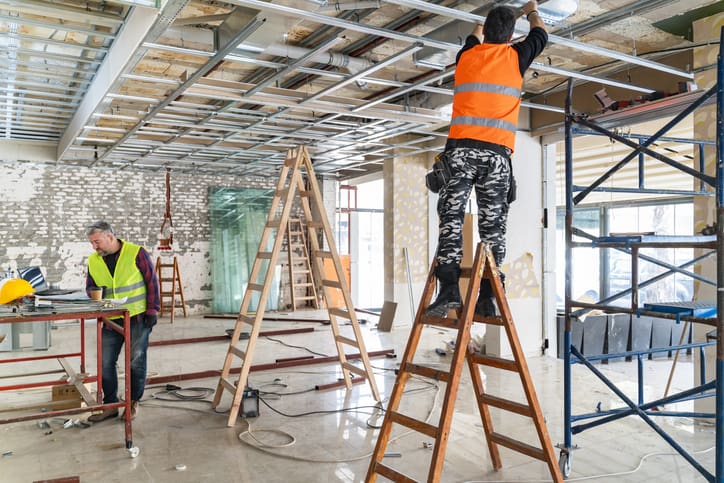 Revised alt text: Construction workers installing ceiling framework and internal building elements inside an unfinished commercial office during a Cat A fit out project.
