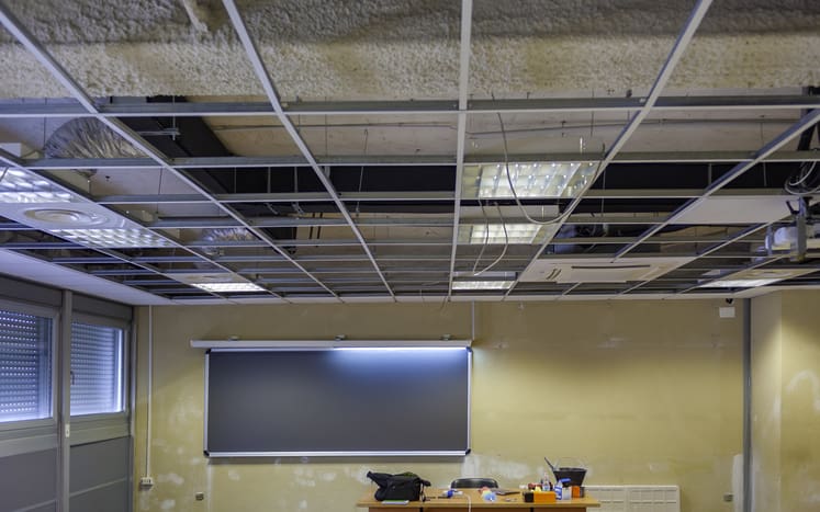 Office interior during a Cat B fit out with a suspended ceiling grid, lighting, ventilation systems and exposed building services being installed.