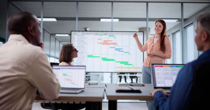 Presenter discussing a detailed project programme and Gantt chart with colleagues during an end to end project management meeting for a workplace project.