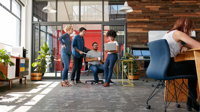 Employees collaborating in a refurbished open-plan office with glass meeting rooms, timber wall finishes, desks, planting and flexible breakout areas